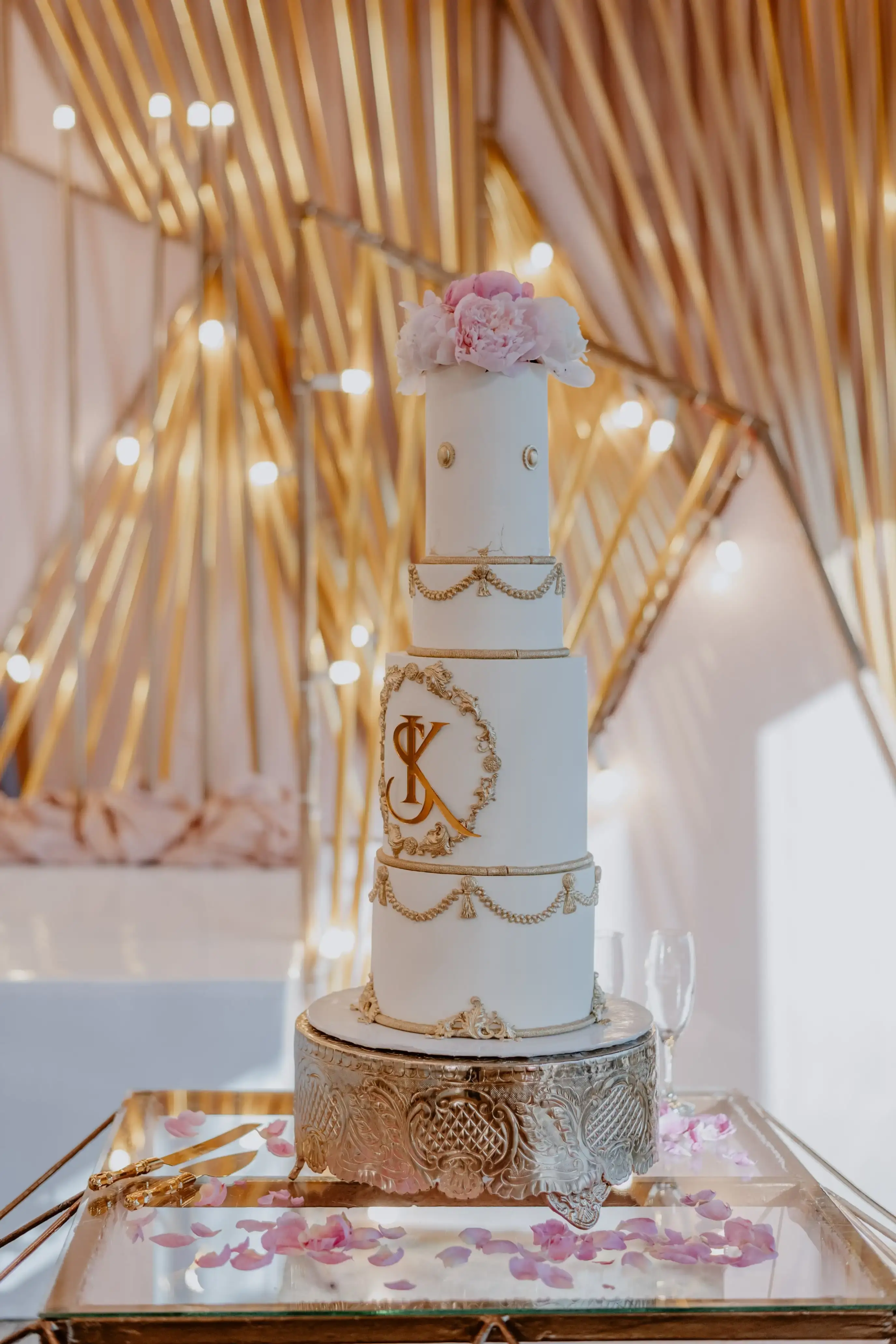 Tall white wedding cake with ornate gold piping, swags and a gold monogram medallion