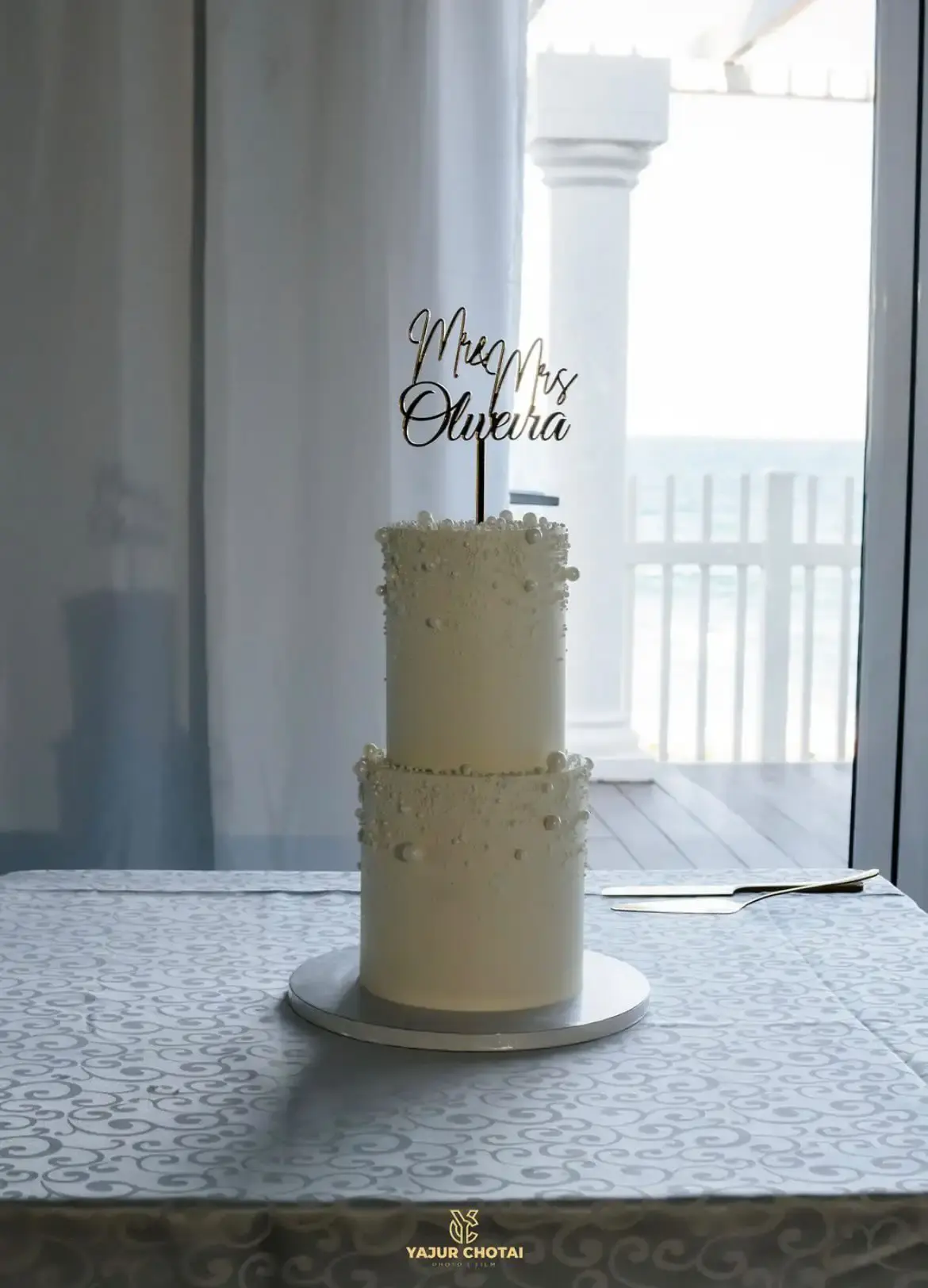 Two-tier white wedding cake finished with pearl clusters and a “Mr & Mrs” script topper
