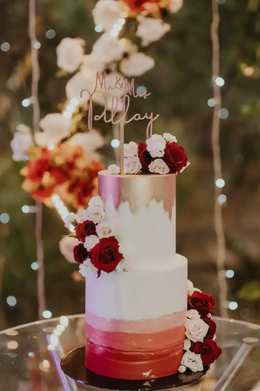 Two-tier wedding cake with a gold-to-white-to-red ombre finish, fresh red and white roses