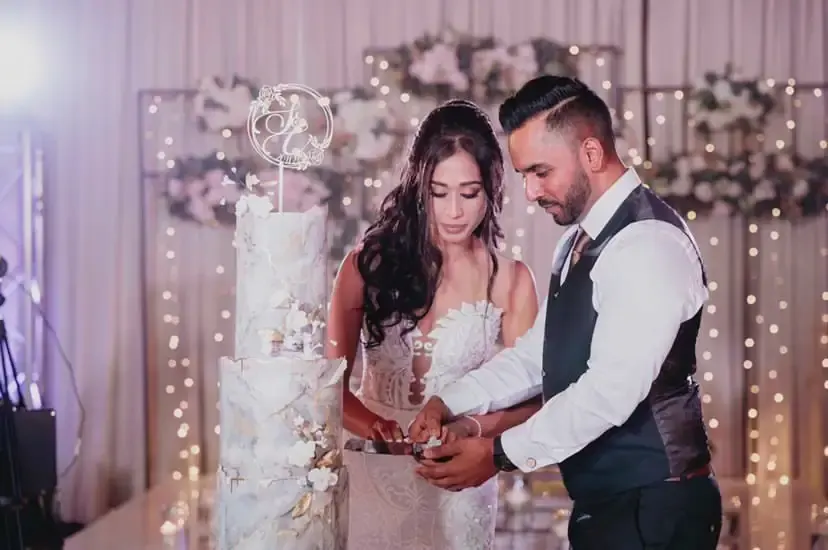 Bride and groom cutting a marble and gold-leaf tiered wedding cake at an indoor reception