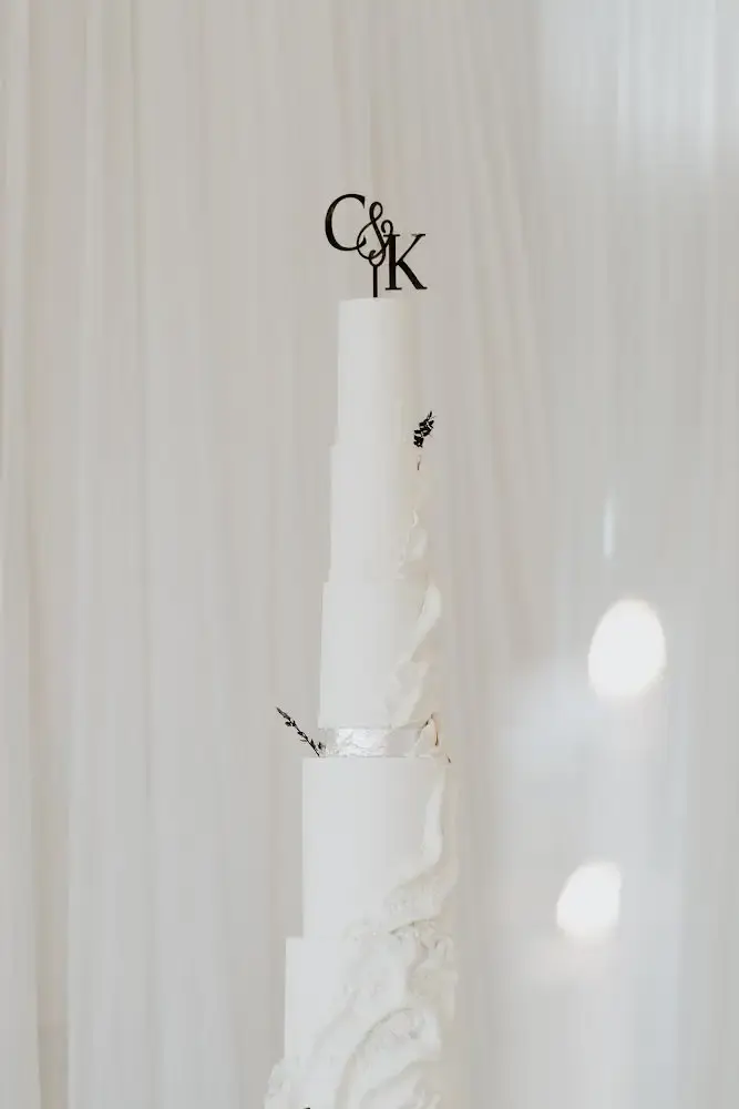 Tall white wedding cake with a sculpted torn-paper texture on the lower tiers and a monogram topper