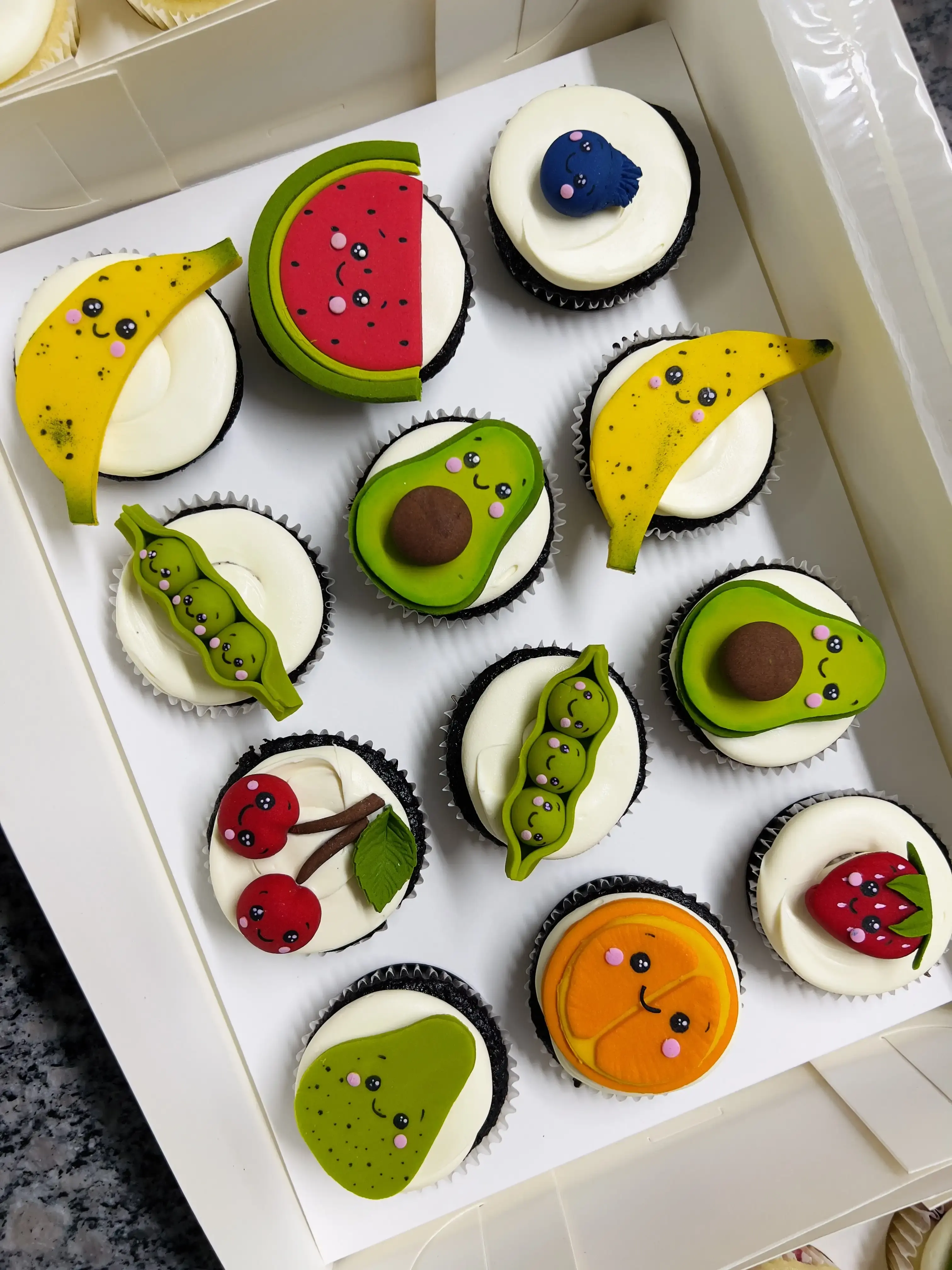 Cupcakes topped with cute cartoon-style fondant fruit — banana, watermelon, avocado, peas, cherries, orange, strawberry, kiwi