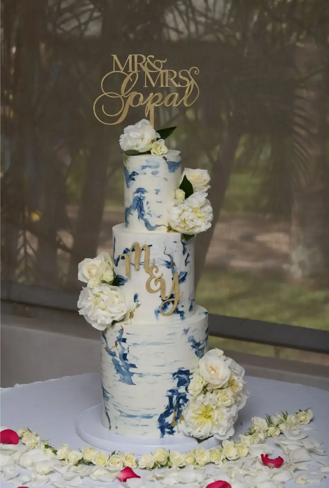 Three-tier wedding cake with a blue watercolour marble finish, white roses and a gold “Mr & Mrs” topper