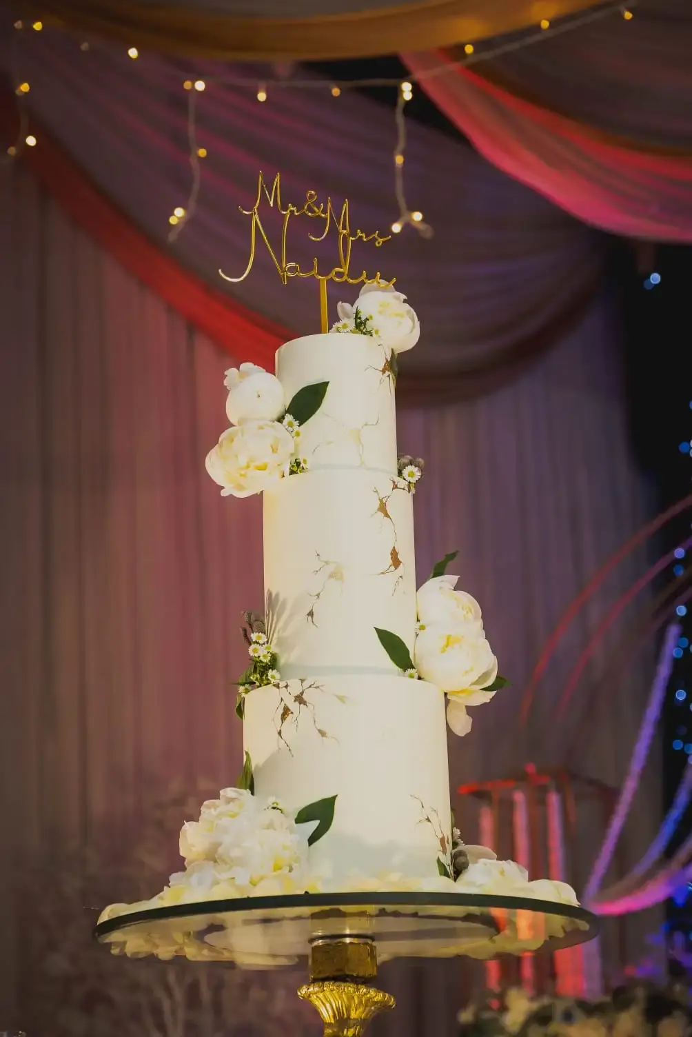 Tall ivory marble wedding cake with cracked gold-leaf detailing and white peonies