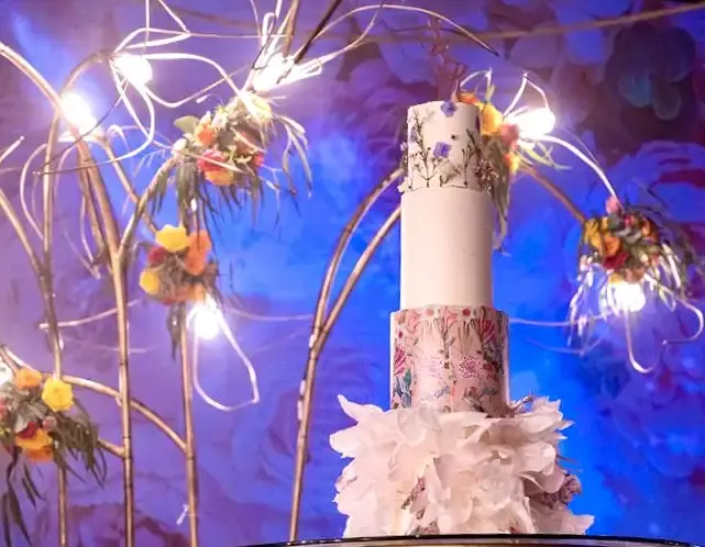 White cake with painted wildflowers under a lit branch installation