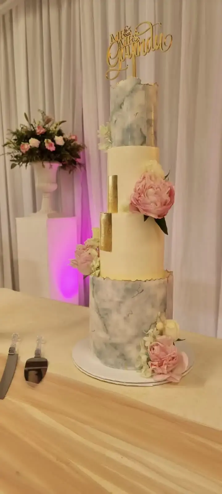Three-tier wedding cake alternating blue-grey marble and gold-edged ivory tiers, with pink peonies