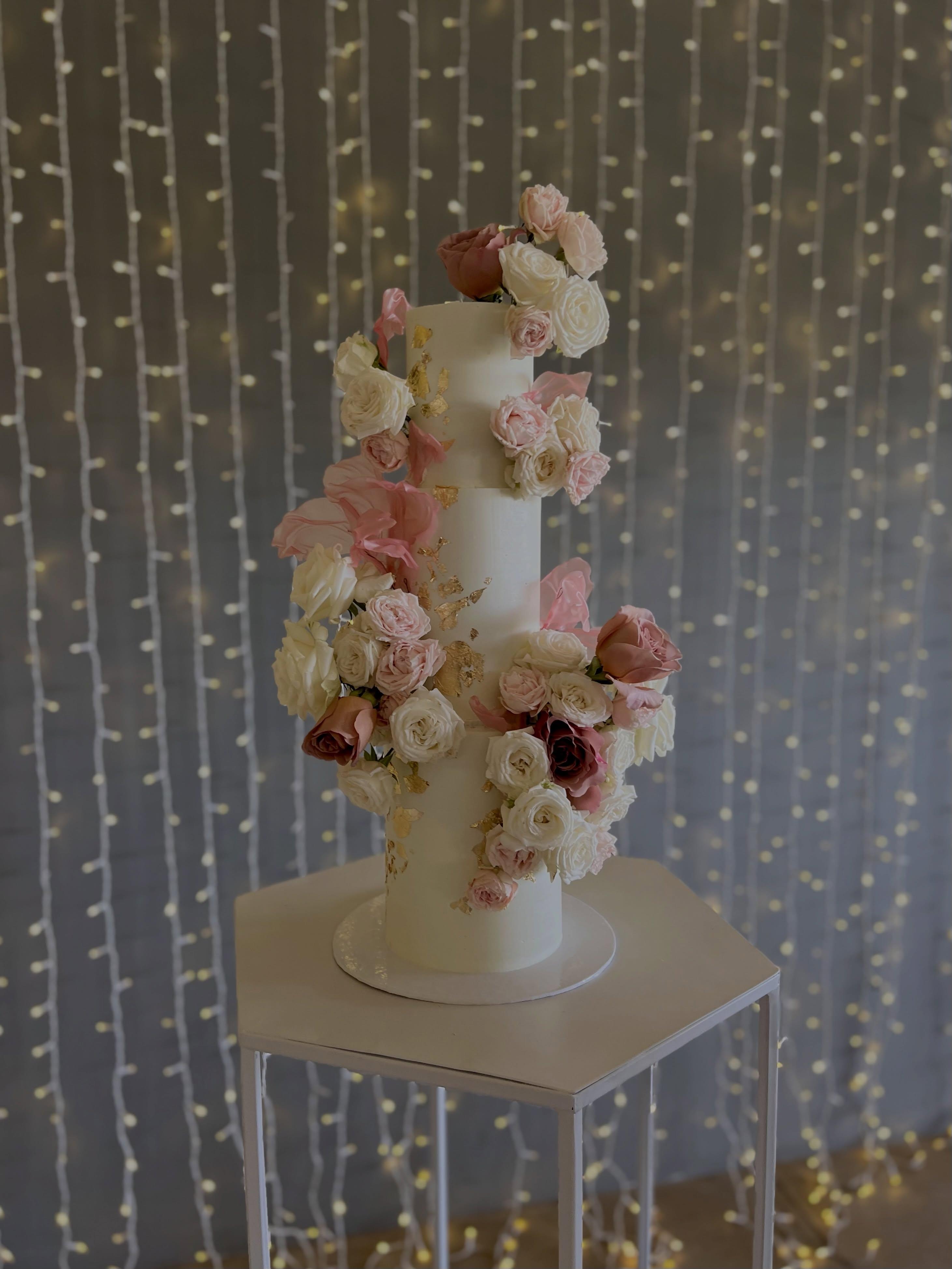 Tall white wedding cake with cascading roses and gold leaf detail