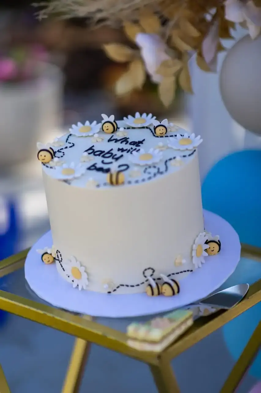 Single-tier baby shower cake with daisy and bee decorations and a “what will baby bee?” message