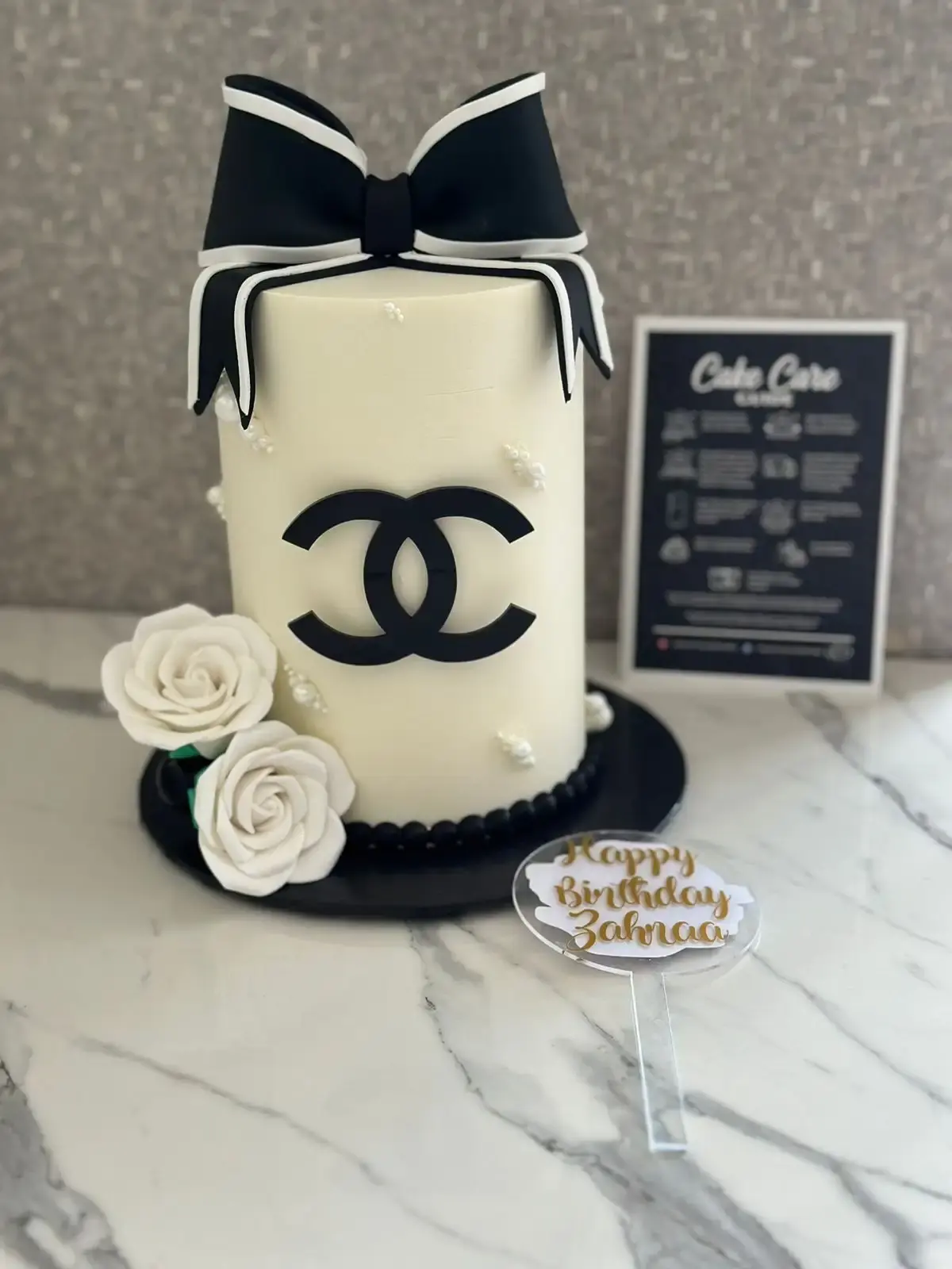 Cream cylinder cake with a black-and-white fondant bow, designer-style plaque and sugar roses